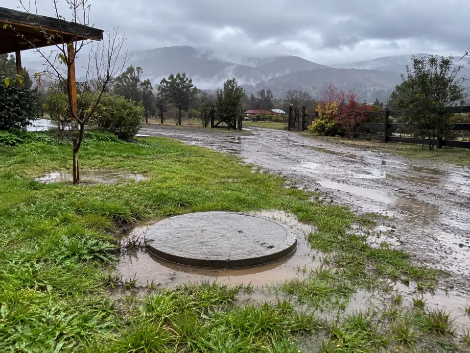 Parcela bajo la lluvia con charcos y agua alrededor de la tapa de la fosa