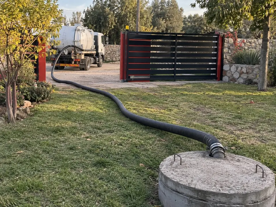 Manguera de succión que cruza el jardín desde el camión, afuera del portón, hasta la tapa de la fosa