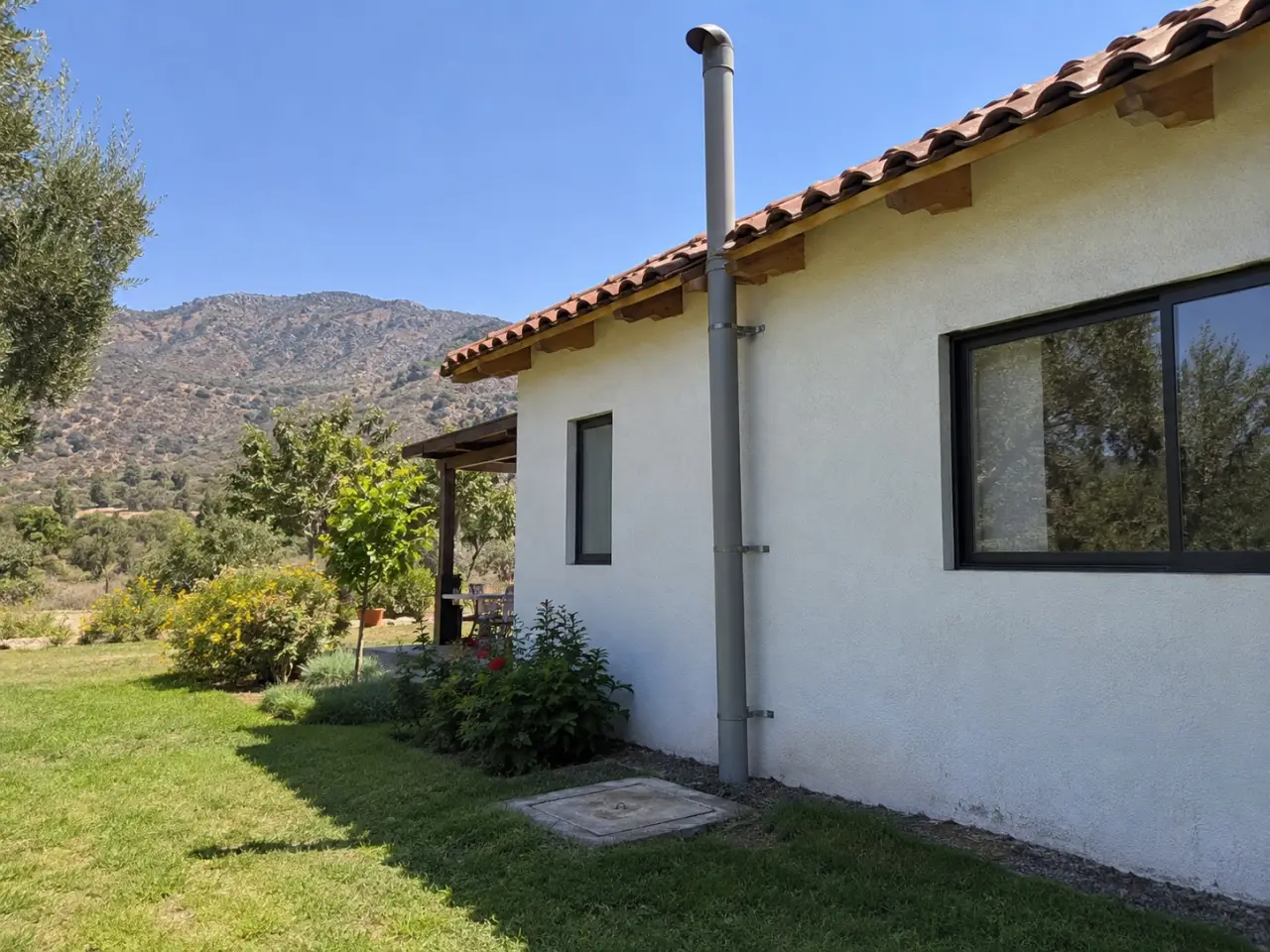Tubo de ventilación que sube por el muro de una casa de campo, con la tapa de la fosa al pie